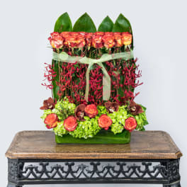 Tropical floral arrangement with orange roses and red orchids in a green vase