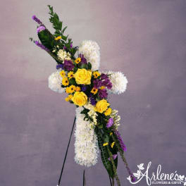 Standing white floral cross with yellow roses and purple flowers on an easel