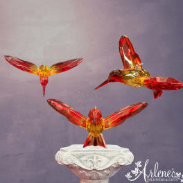 Three crystal hummingbird figurines on a decorative pedestal