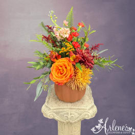 Mixed orange, red, and yellow flowers arranged in a pumpkin-shaped vase