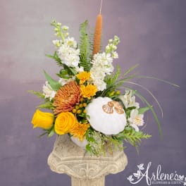 Floral arrangement with yellow and white flowers in a decorative pumpkin container