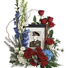 Floral tribute around a framed military portrait with red roses and blue-white flowers