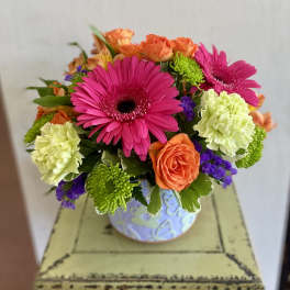 Bright mixed bouquet in a patterned vase with pink gerberas and orange roses