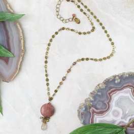 Beaded necklace with a pink pendant on a white surface beside agate slices