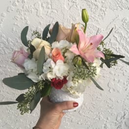 Handheld bouquet of pink lilies, roses, and white hydrangeas in a white vase