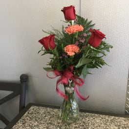 Red roses and orange carnations in a glass vase with a pink ribbon