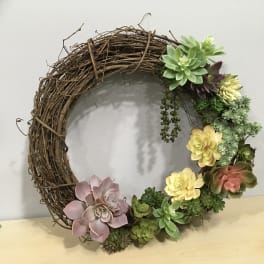 Succulent wreath on a grapevine ring with pink, yellow, and green rosettes