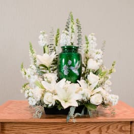 White lilies and roses arranged around a green urn centerpiece