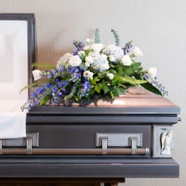 White and blue floral casket spray on a dark casket