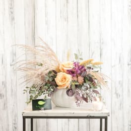 Peach roses and purple flowers in a white vase with airy dried grass