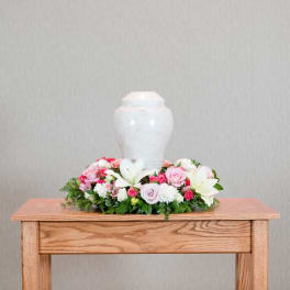 Pink and white floral arrangement around a white urn on a wooden table
