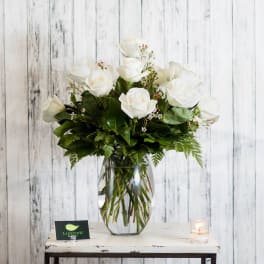 White roses arranged in a clear glass vase with greenery