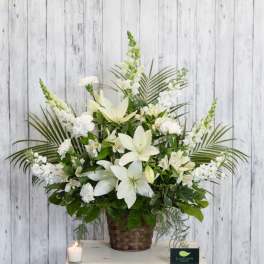 White floral arrangement in a woven basket with a candle beside it