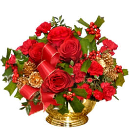 Red roses and carnations with holly, red ribbon, and gold pinecones in a gold bowl.