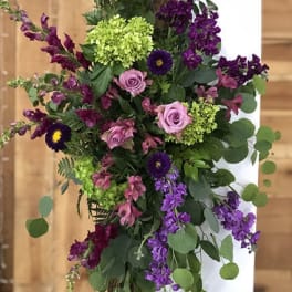 Asymmetrical purple and pink flower spray with green hydrangeas cascading from a wooden post.