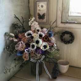 Mixed bouquet in a glass vase with roses, anemones, and dark accents