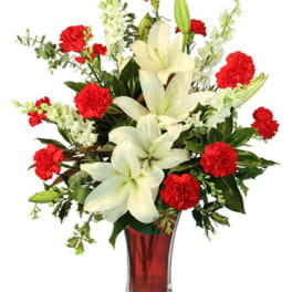 White lilies and red carnations in a red glass vase