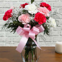 Pink and white carnations in a glass vase with a pink ribbon