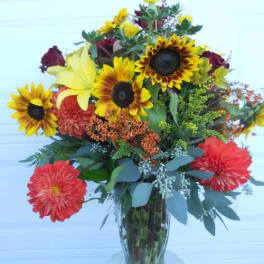 Mixed bouquet with sunflowers, lilies, and red dahlias in a glass vase