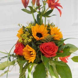 Bouquet of orange lilies, sunflowers, and red roses in a glass vase