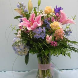 Mixed bouquet of pink lilies, roses, and blue flowers in a glass vase