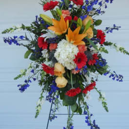 Tall mixed floral spray with orange lilies, red daisies, and blue flowers on an easel