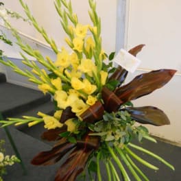 Tall yellow floral arrangement with long stems and dark red leaves
