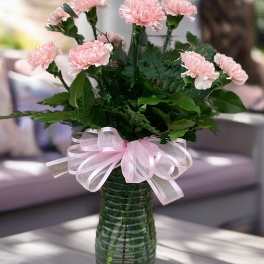 Pink carnations in a green glass vase with a pink ribbon bow