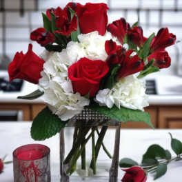 Red roses and white hydrangeas in a glass vase with a candle nearby