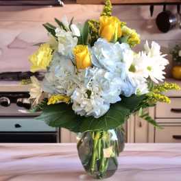 Bouquet of yellow roses, blue hydrangeas, and white daisies in a glass vase