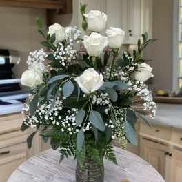 White roses arranged in a glass vase with baby's breath and greenery