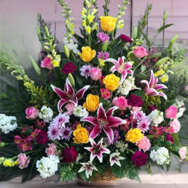 Large mixed floral arrangement with yellow roses, pink lilies, and white blooms in a basket