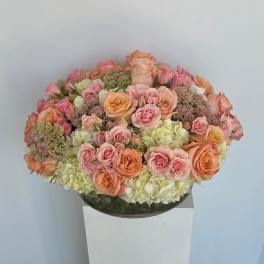 Round bouquet of pink and peach roses with pale hydrangeas in a glass bowl