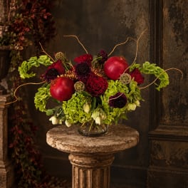 Red roses and green hydrangeas arranged in a glass vase with pomegranates