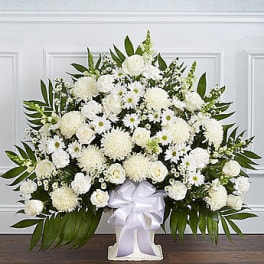 White floral standing spray with a white ribbon on a pedestal vase