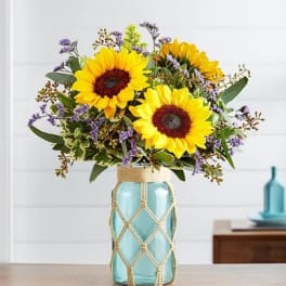 Sunflowers arranged in a blue glass vase with purple filler flowers