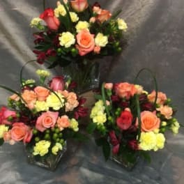 Three mixed flower arrangements with pink and peach roses in clear vases
