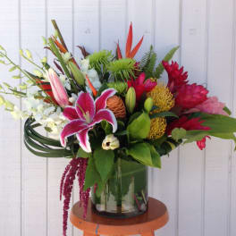 Tropical bouquet with pink lily, red blooms, and orchids in a glass vase