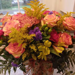 Bouquet of pink roses, yellow flowers, and purple accents in a glass vase