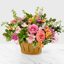 Mixed bouquet of pink and peach flowers in a wooden basket