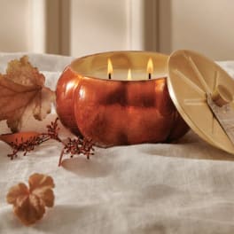 Copper candle with lid and autumn leaves on a white fabric surface