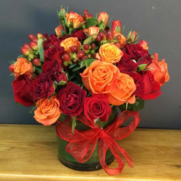 Bouquet of red and orange roses in a glass vase with a red ribbon
