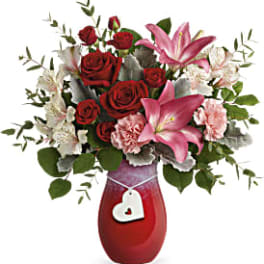 Red roses and pink lilies in a red vase with a heart charm