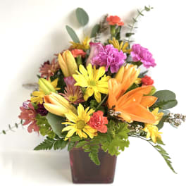 Mixed bouquet in a square vase with orange lilies and yellow daisies