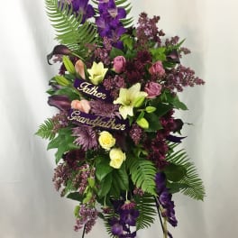 Tall funeral spray with purple flowers and ribbons reading Father and Grandfather