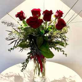 Red roses arranged in a clear glass vase with greenery