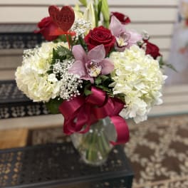 Bouquet of red roses, white hydrangeas, and pink orchids in a glass vase