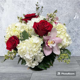 Bouquet of red roses, white hydrangeas, and a pink orchid in a low vase