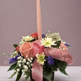 Pink candle in a mixed flower arrangement with a striped ribbon