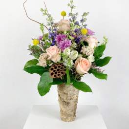 Mixed bouquet of roses, purple blooms, and yellow accents in a birch-style vase